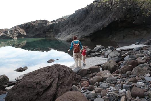 Tourists enjoying a tranquil natural pool reflecting the sky, surrounded by volcanic rocks in the azores