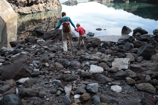 Mother and son walking on rocks near calm water, enjoying a tranquil moment in nature