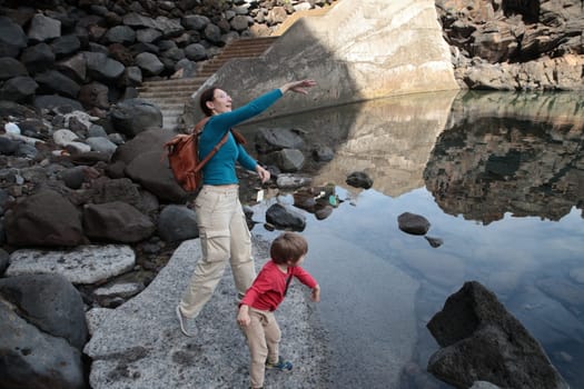 Tourist and child enjoying natural pool in rocky volcanic landscape, exploring nature during vacation