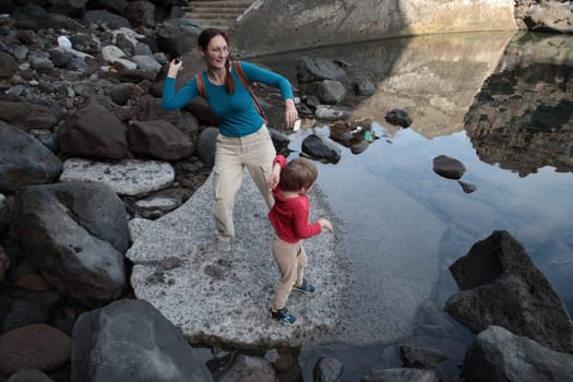 Mother and son enjoying a leisurely afternoon throwing stones into a calm lake surrounded by rocks