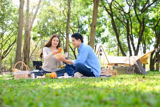 Happy couple enjoying picnic meal together while camping in a forest.