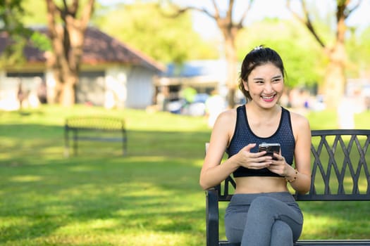 Athletic woman relaxing in the park with mobile phone taking a break after exercising.