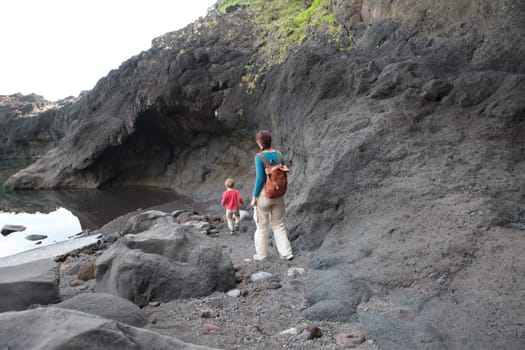 Tourists walking on rocky volcanic beach near sea cave in madeira island, portugal