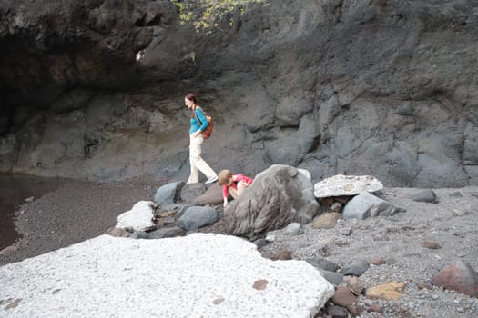 Mother and son walking along a rocky beach, exploring volcanic caves and enjoying the natural landscape