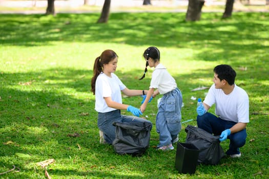 Happy family picking up litter together in a park for environmental conservation.
