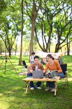 Happy couple using laptop while camping with their daughter in the background.