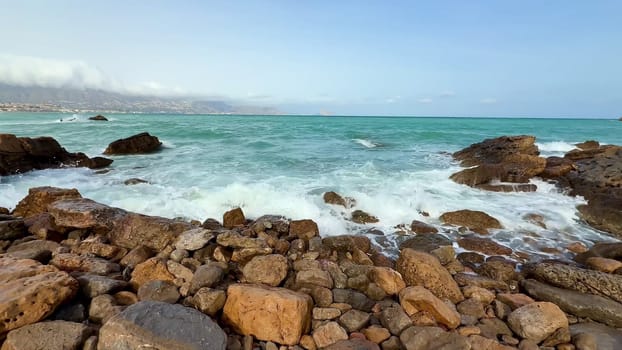 Enjoy the stunning view of ocean waves gently crashing against the rocky coastline under a clear blue sky