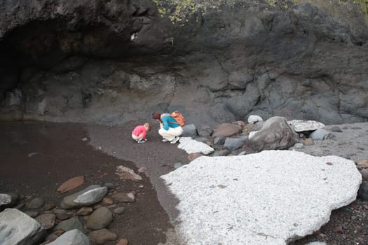 Mother and child exploring a volcanic beach with black sand and white rocks
