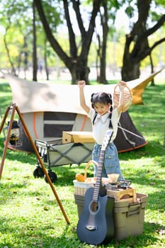 Cheerful asian girl enjoying outdoor adventure at a campsite.