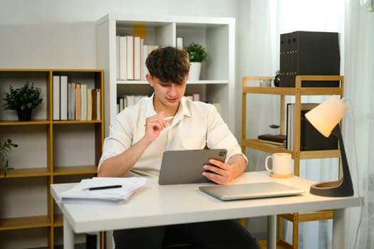 Caucasian man working on a digital tablet with a stylus pen in a home office.