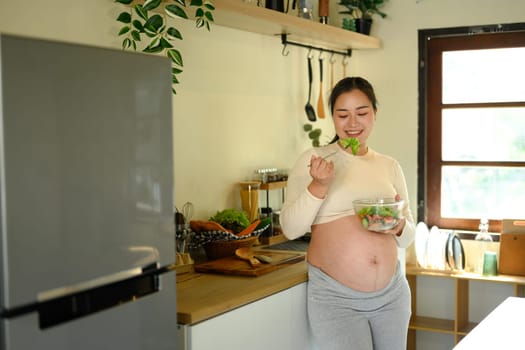 Happy pregnant woman eating a fresh salad, promoting healthy eating habits during pregnancy.