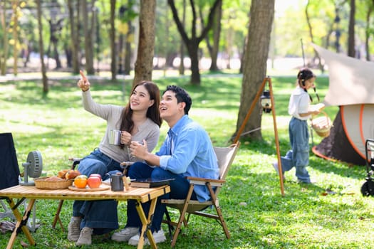 Relaxed family sitting outdoors at a campsite surrounded by trees and fresh greenery.