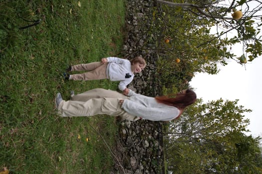 Mother and son holding hands, enjoying a moment together in a picturesque lemon orchard next to a stone wall