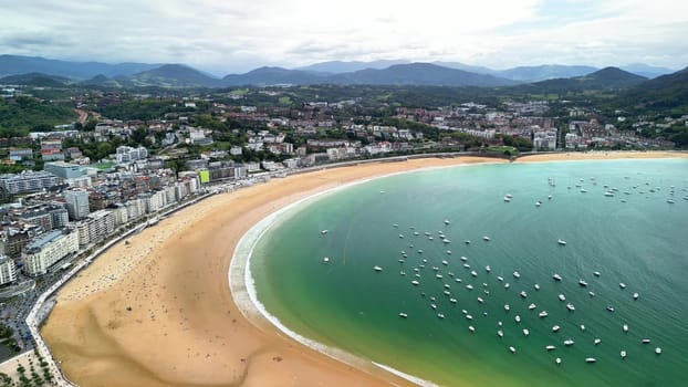An aerial view shows a vibrant coastal town, its beautiful beach, and colorful boats on turquoise waters