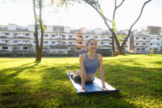 Beautiful woman practicing yoga in cobra pose on mat at a peaceful park.