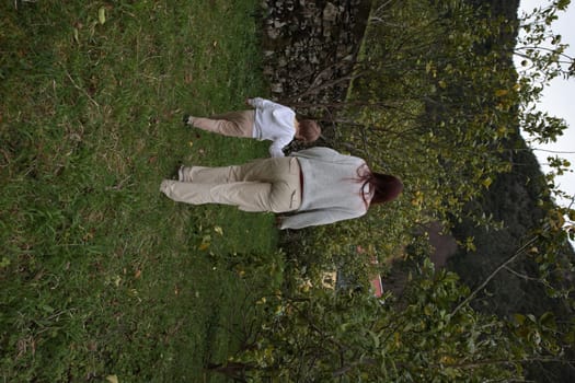 Mother and her son enjoying a walk in nature, exploring the grassy area near apple trees