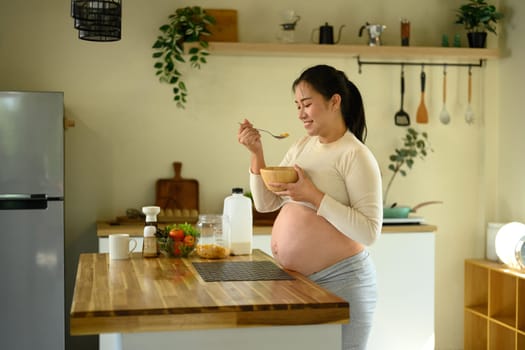 Smiling pregnant woman enjoying a bowl of corn flakes. Healthy pregnancy lifestyle concept.