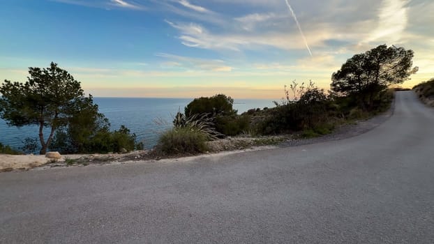 A stunning view of a winding coastal road next to the sparkling ocean, enhanced by a captivating sunset
