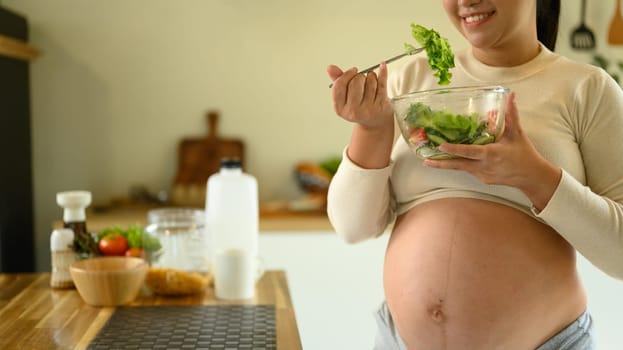 Happy pregnant woman eating a fresh salad, promoting healthy eating habits during pregnancy.