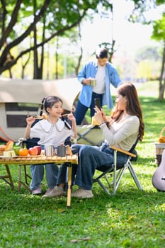 Happy mother and child seated near a tent enjoying time while camping under the trees.
