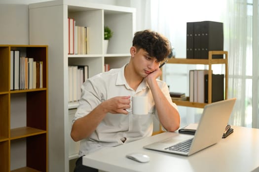 Bored businessman staring at laptop screen during a slow workday in modern home office.