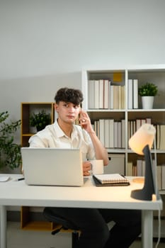 Caucasian young entrepreneur using his laptop while talking on mobile phone at workplace.