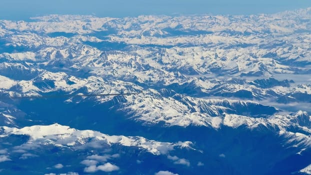 A breathtaking aerial view showcasing stunning, majestic, snowcapped mountain ranges beneath clear blue skies