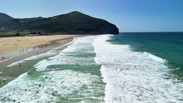 This aerial view shows a vibrant beach where surfers enjoy the waves under sunny skies in a scene of fun