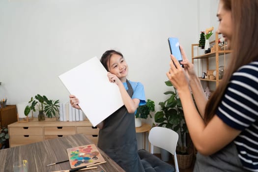 A mother captures a joyful moment of her daughter holding a canvas during family time, celebrating creativity in an art studio.