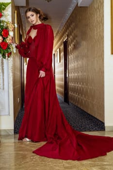 Model in red dress, elegant young woman in long evening dress. Beautiful girl with high hairstyle, shooting in hotel.