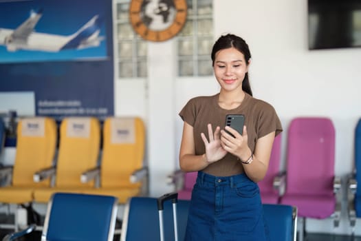 A young woman smiling while using her smartphone in an airport waiting area, expressing anticipation and joy during her travels.