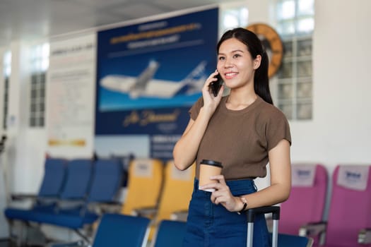 A cheerful young woman speaking on her smartphone while holding a cup of coffee at the airport, embodying the spirit of travel adventure.