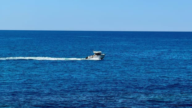 A sleek speedboat is elegantly slicing through the tranquil, blue ocean waters on a beautiful, sunny day