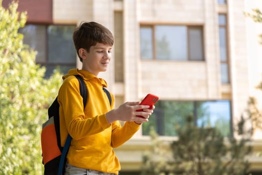 Teenage boy in front of an apartment building looks at his smartphone and smiles. Captures happiness from online communication, chatting with friends, and staying connected.