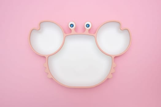 Cute children's plate in crab shape on pink background. Serving baby. Concept for kids menu, nutrition and feeding. Funny bowl.