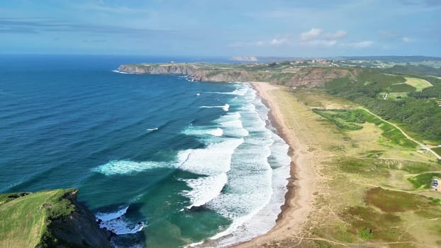A stunning aerial shot beautifully capturing waves crashing energetically on the shore with lush green hills nearby