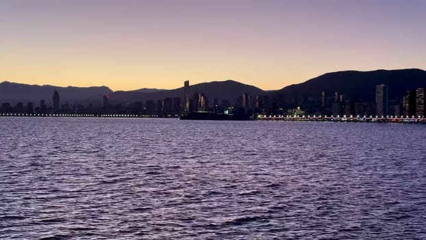 Enjoy a stunning sunset view showcasing tranquil waters accompanied by a beautifully illuminated skyline backdrop