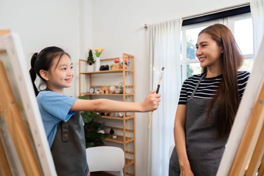 A girl excitedly shares a paintbrush with her mother during family time, fostering creativity and joy in a cozy art space.