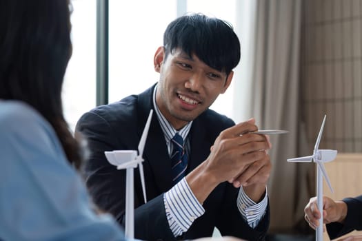 A man consulting with colleagues about sustainable energy solutions using wind turbine models, enhancing ESG strategies during their meeting.