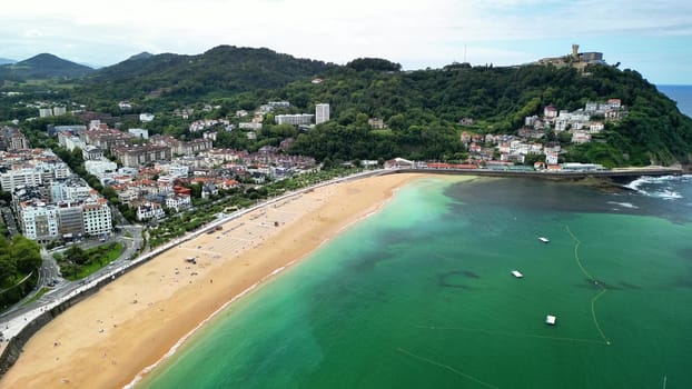 This aerial shot captures a charming coastal town by a sandy beach and the vibrant blue ocean waters