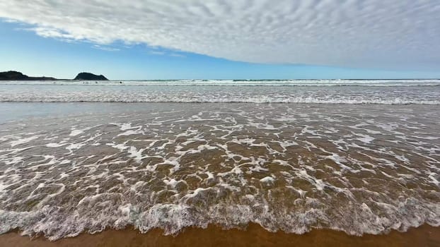 This scene captures a tranquil beach featuring gently rolling waves under a beautiful, peaceful, cloudy sky
