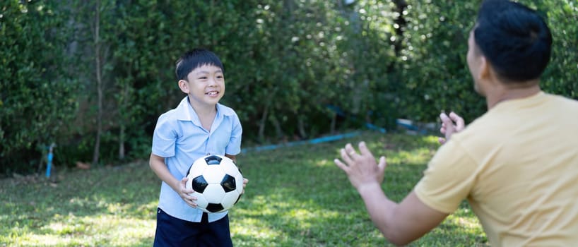 A young boy, smiling and engaging with his father as they toss a soccer ball, promoting wellness through active play and family interactions.