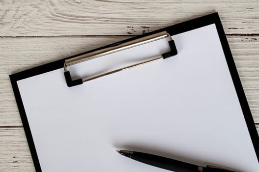 Top view of a blank clipboard with a sheet of white paper and a black pen. Copy space concept.