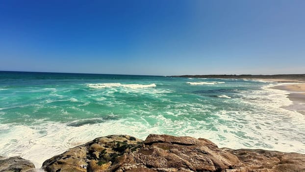 A stunning coastal scene showcasing vibrant turquoise waters and gleaming sunlit rocks on a beautiful day