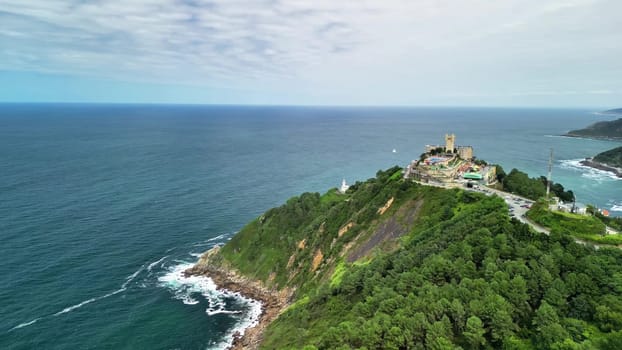 An aerial view of a stunning coastal landscape with vibrant greenery and an intriguing historical structure