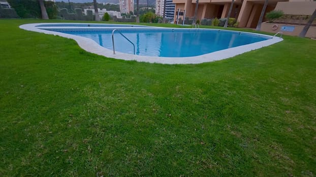 A serene swimming pool is surrounded by a vibrant green lawn in a modern residential area, offering comfort