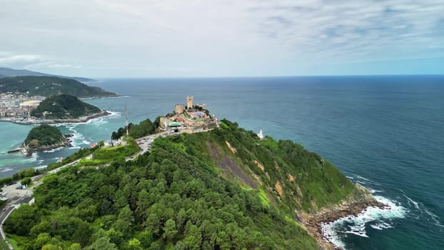 An aerial photo captures lush greenery, a beautiful coastline, and a historic structure by the vast ocean