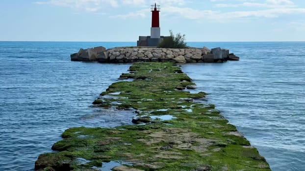 A stunning lighthouse stands atop a rugged jetty, surrounded by calm blue waters and vibrant greenery