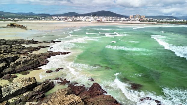 Witness the breathtaking aerial views of a pristine beach embellished with turquoise waves and a rugged rocky shoreline