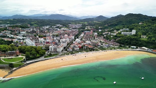 Aerial view of a vibrant coastal town by the beach, surrounded by lush green hills in the background